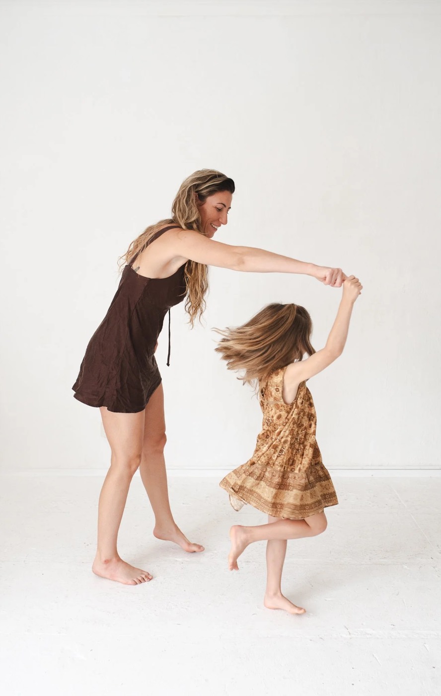 A clinician and a child dancing together in a bright studio, mid-movement and laughing.
