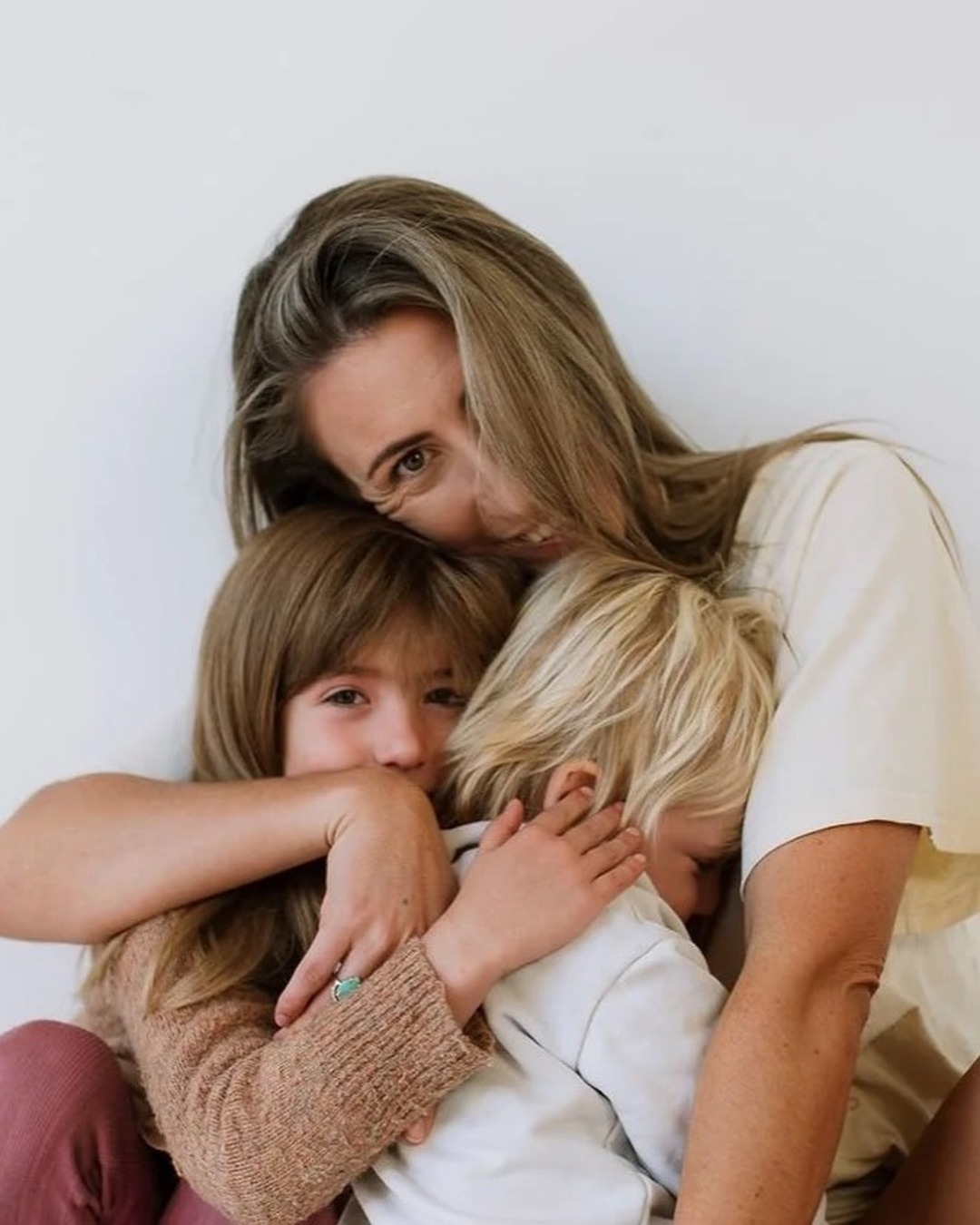 A parent holding two children close in a bright, calm studio, a moment of warmth and connection.